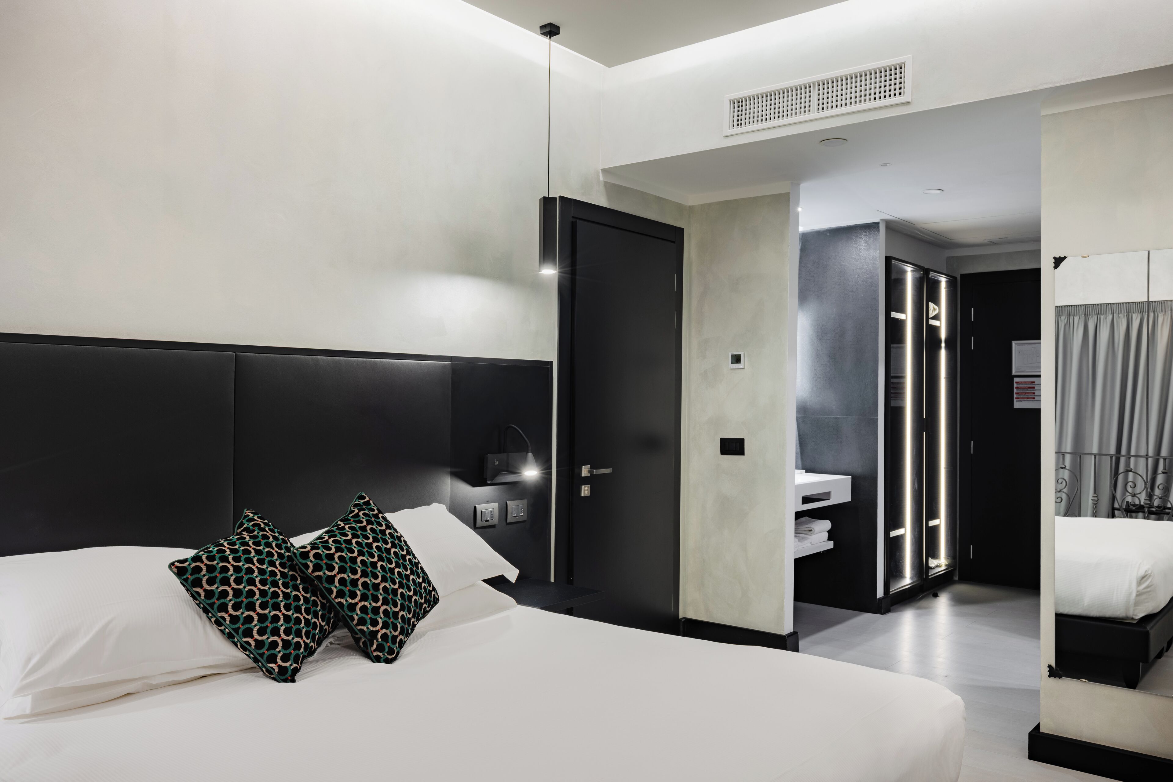 Ein modernes Hotelzimmer mit einem großen Bett, einem Nachttisch, einem Kleiderschrank und einem durchgegangene Tür sichtbaren Badezimmer.