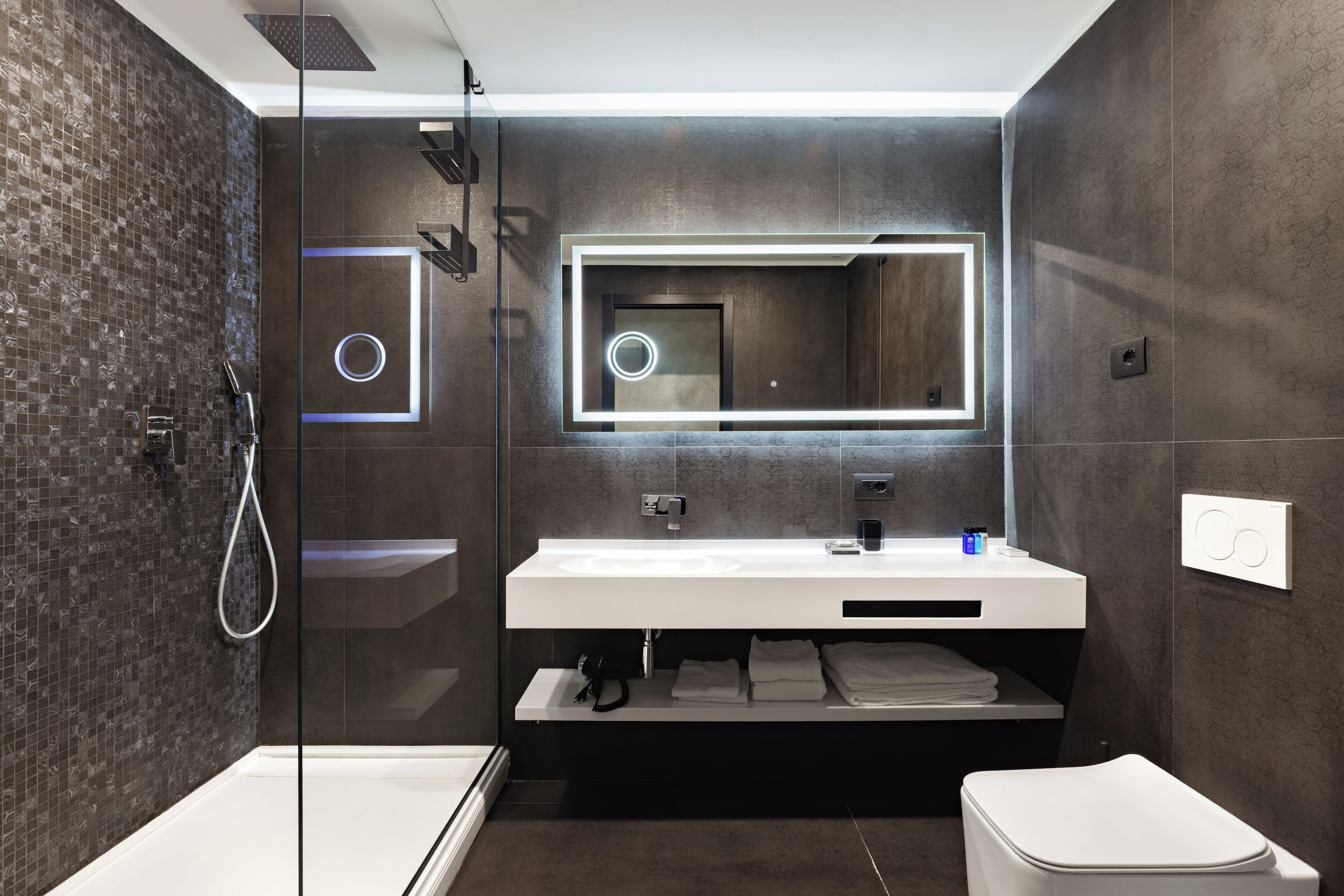 Un baño moderno con ducha envuelta en vidrio, un espejo grande y un tocador blanco.