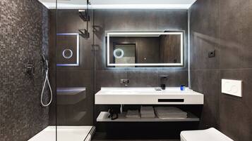 Un baño moderno con ducha envuelta en vidrio, un espejo grande y un tocador blanco.