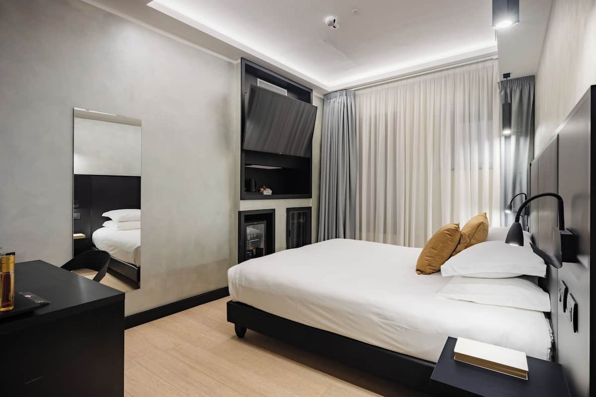 Una habitación de hotel moderna con una cama grande, un escritorio, un espejo y un televisor.