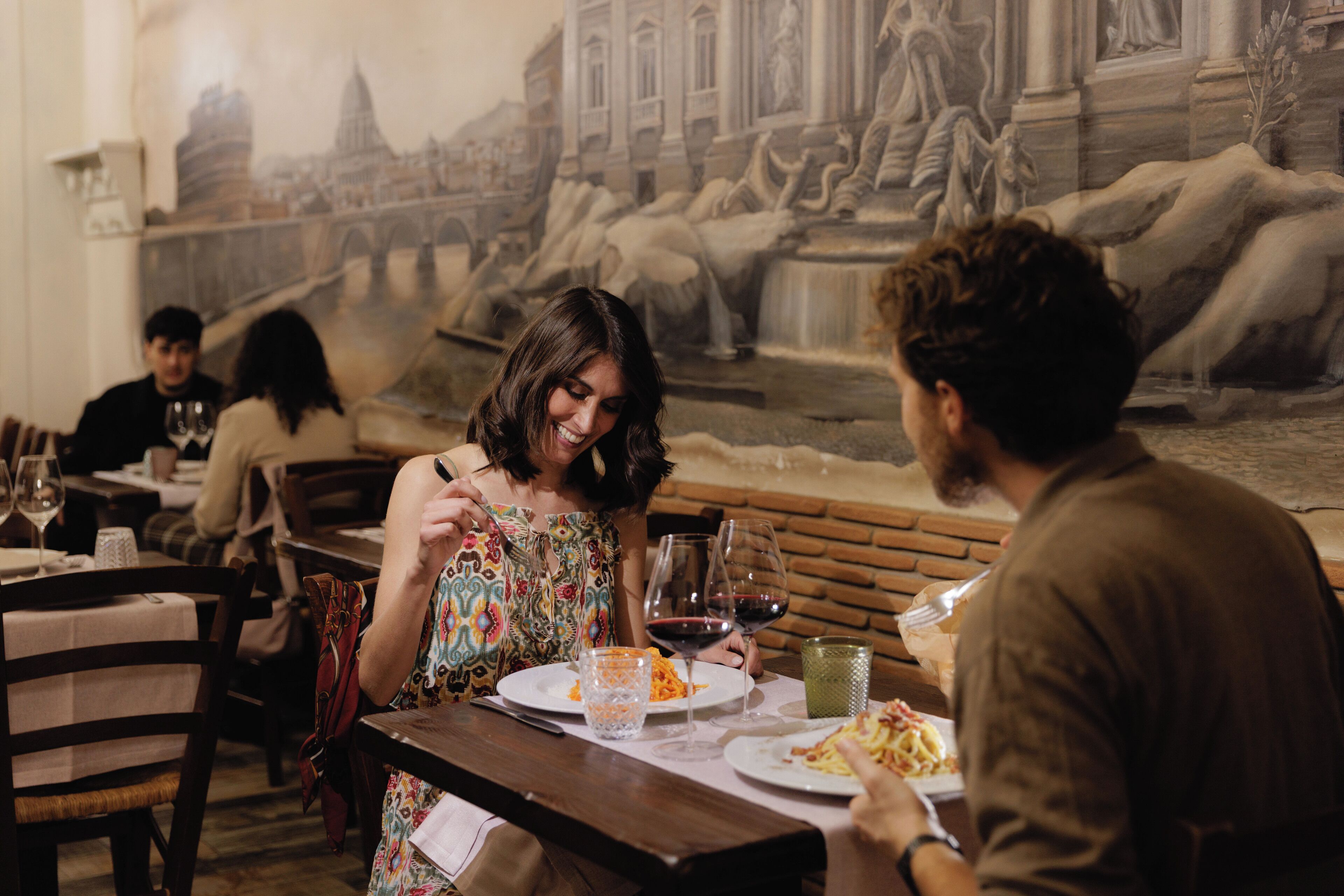 Un comedor con un mural de un paisaje urbano histórico, mesas y sillas de madera.