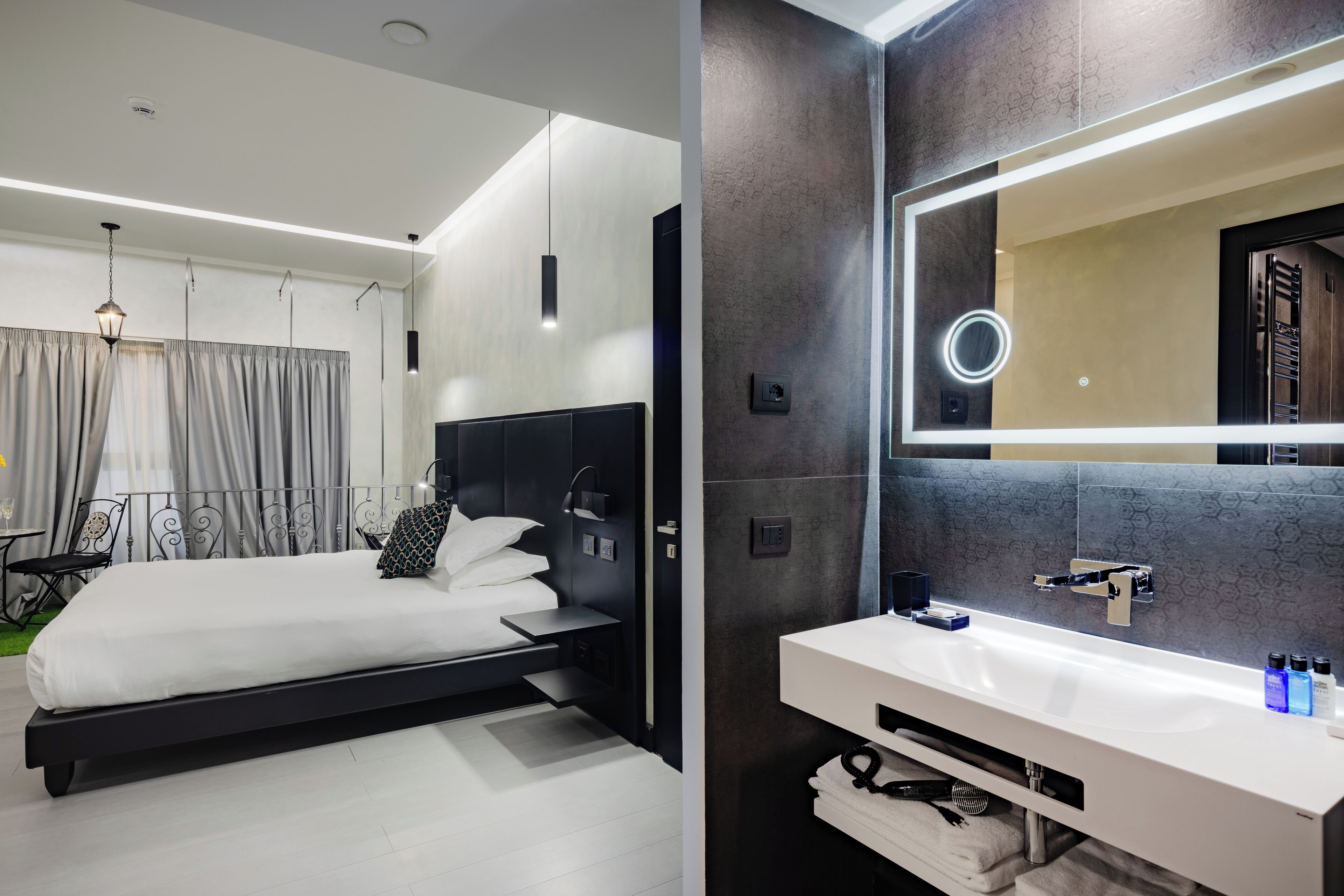 Une chambre moderne avec un grand lit, des tables de chevet et une coiffeuse intégrée dotée d’un miroir et d’un lavabo.