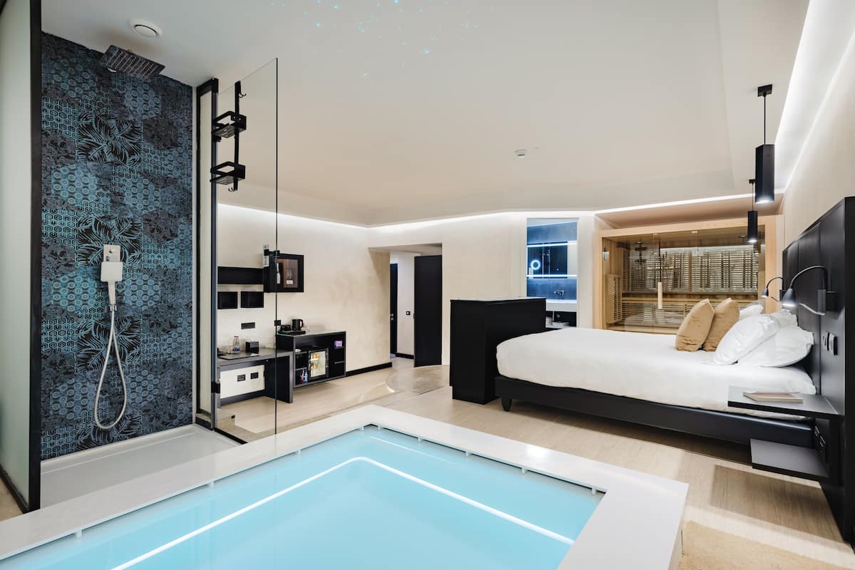 Un dormitorio moderno con una cama grande, un escritorio empotrado y un baño pequeño con ducha.