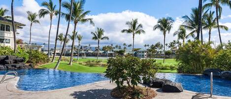 A resort with a swimming pool, palm trees, and a golf course.