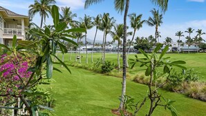 Un campo de golf bien cuidado con palmeras, una piscina y un edificio de fachada blanca.