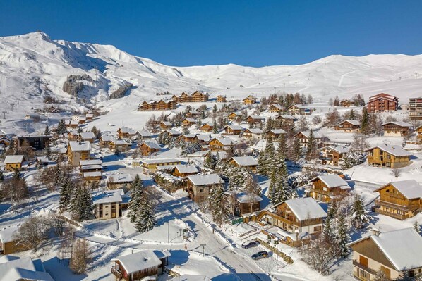 Un pueblo cubierto de nieve con edificios de madera, una pista de esquí y una montaña al fondo.