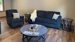 Ein Wohnzimmer mit einem dunkelgrauen Sofa, zwei Sesseln, einem runden Couchtisch und einem kleinen Beistelltisch.