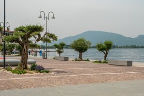 Eine Uferpromenade mit Bäumen, Bänken und Blick auf Wasser und Berge.