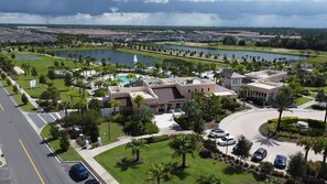 An aerial view of a resort with a swimming pool, tennis courts, and a large lake.