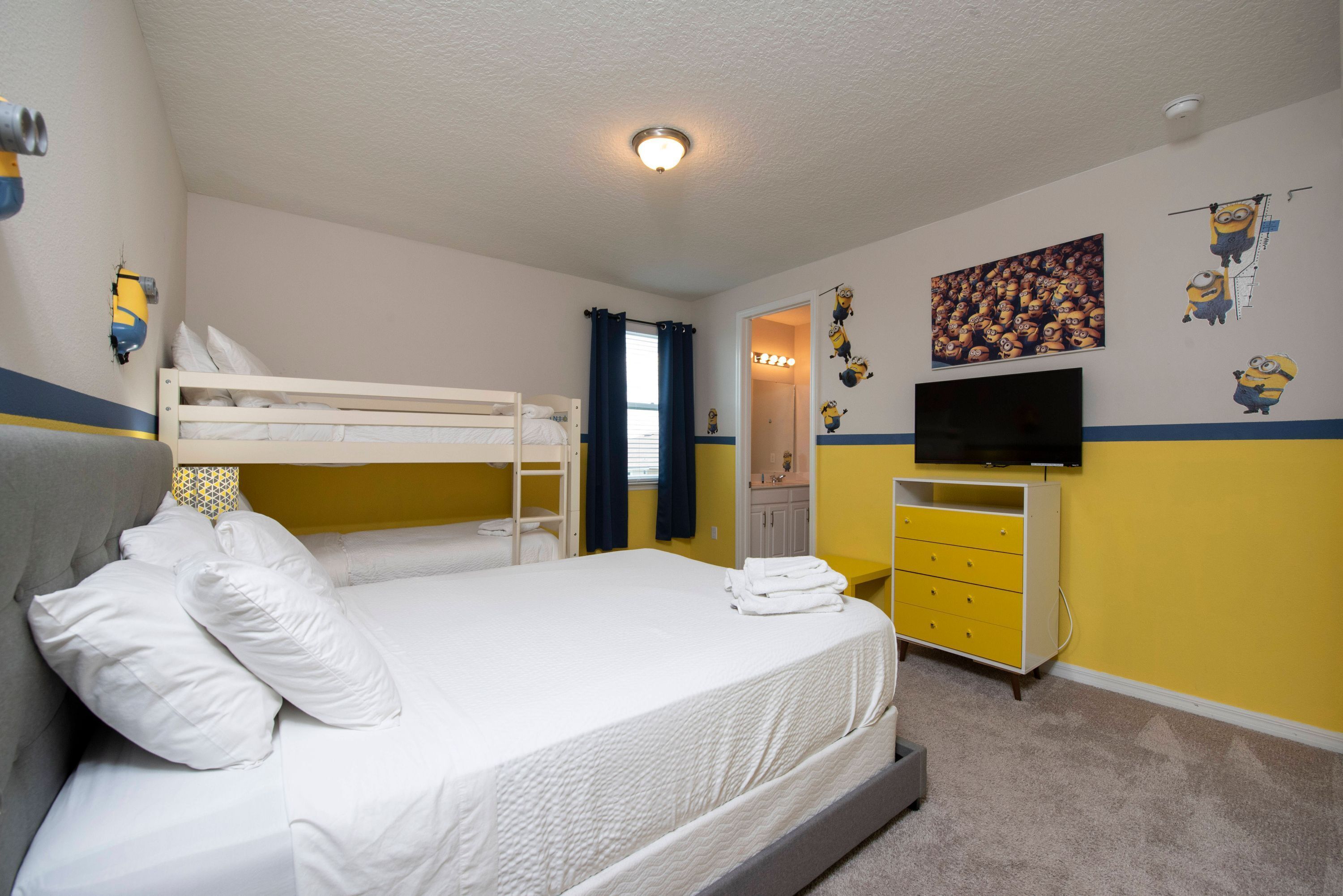 A bedroom with bunk beds, a flat-screen TV, a vanity with a mirror, and Minion-themed wall decals.