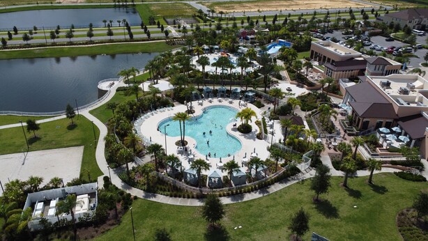 Vista aérea de un complejo turístico con una piscina central, rodeado de palmeras y zonas de descanso.