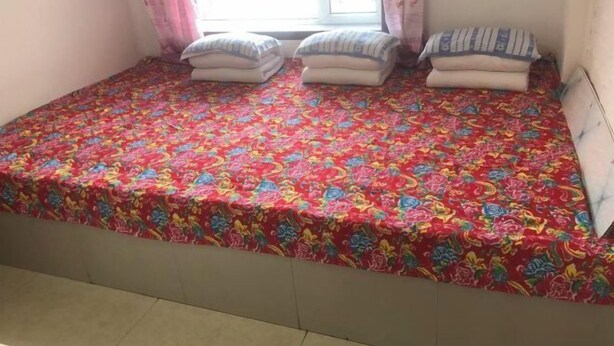 A bed with a colorful floral bedspread, pillows, and a window with curtains. - Mohe Yujia Inn (Mohe)