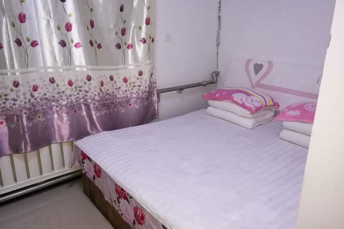 A bedroom with a bed, a curtain, a radiator, and a wall with a heart-shaped decoration.