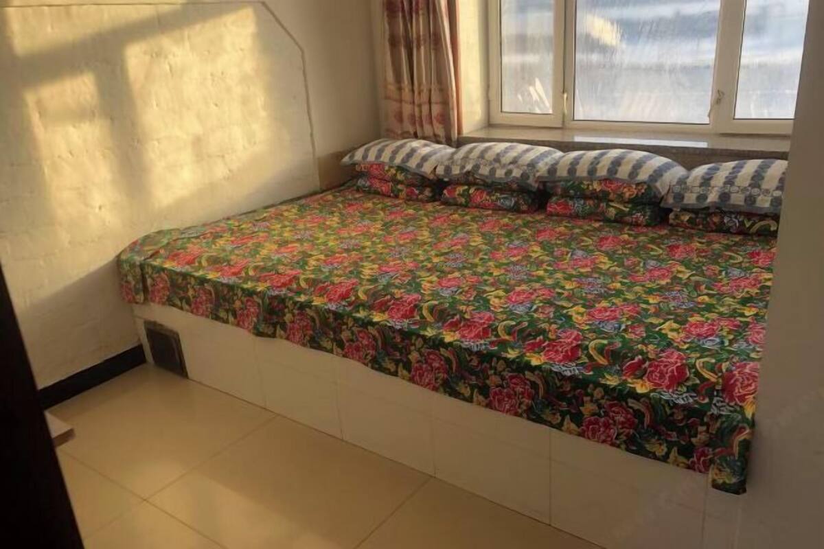 Een slaapkamer met een bloemenbedekking, een raam met gordijnen en een betegelde vloer.