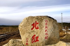 A large rock with red Chinese characters, surrounded by a natural landscape with a distant power line tower. - Mohe Yujia Inn (Mohe)