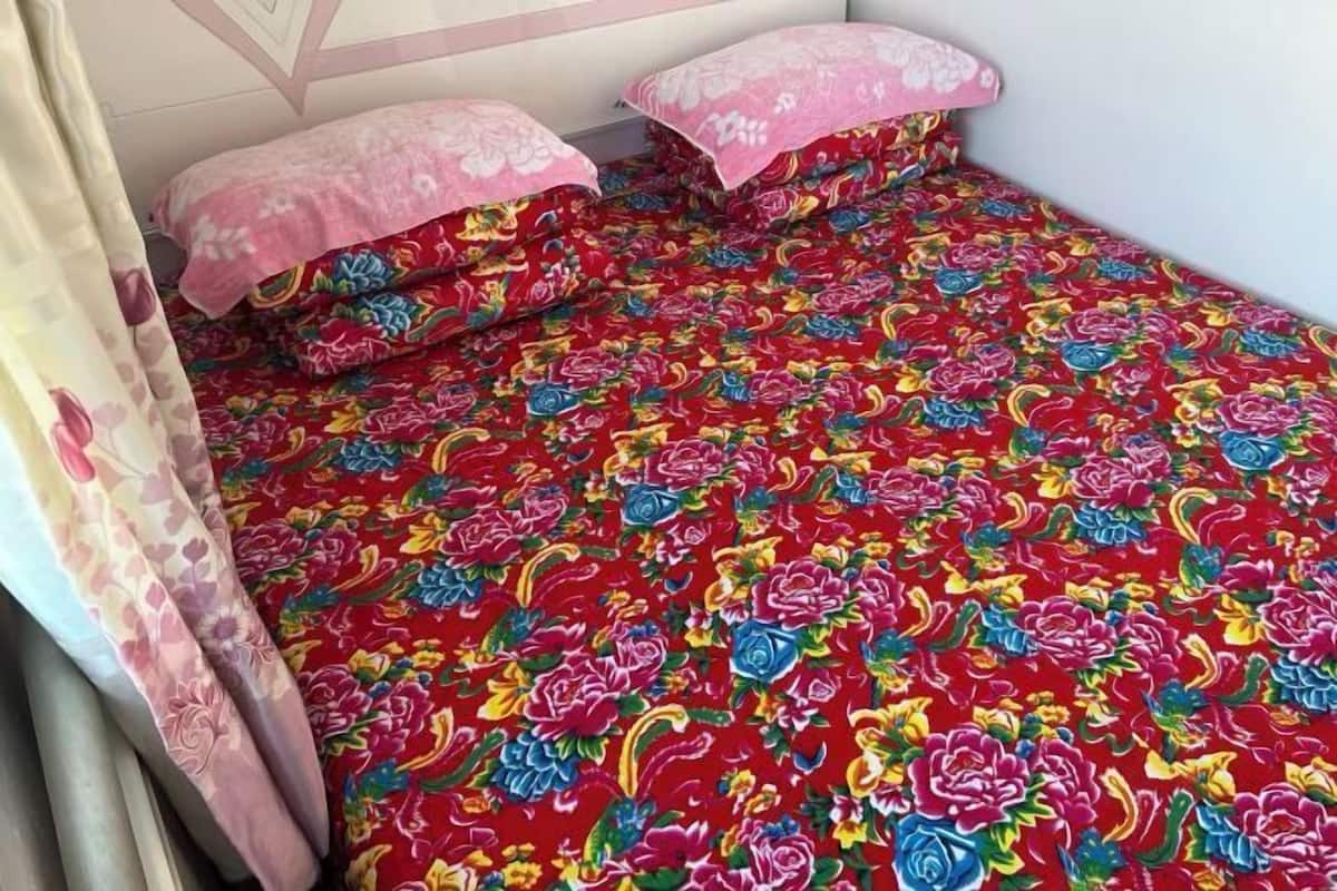 A small bed with floral bedding, a curtain, and a wall with a geometric pattern.