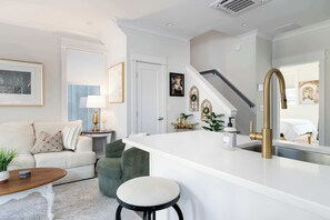 A modern kitchen with a white countertop, a gold faucet, and a large mirror. - Flourish at The Cove Riverwalk Villas (Wilmington)