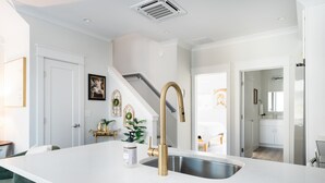 A modern kitchen with a white countertop, a gold faucet, and a stainless steel sink. - Flourish at The Cove Riverwalk Villas (Wilmington)