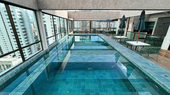 A modern indoor swimming pool with clear glass walls, multiple levels, and outdoor seating areas. - Rooftop.470 Recife by Carpediem (Recife)