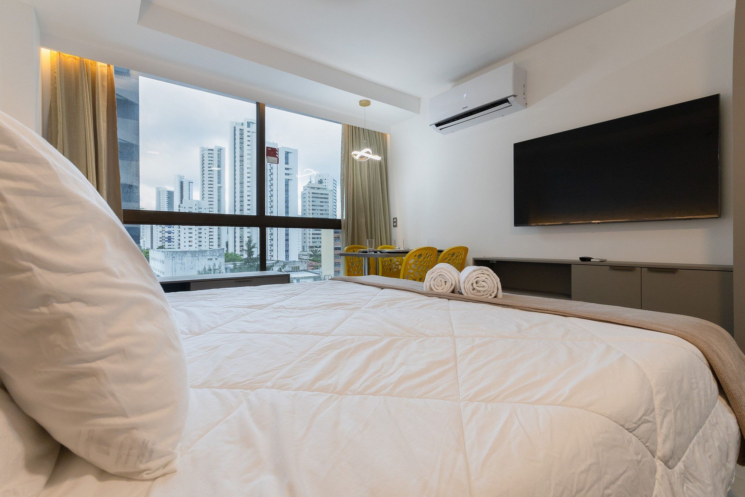 Quarto de hotel moderno com uma cama grande, televisão de tela plana e vista para a cidade.