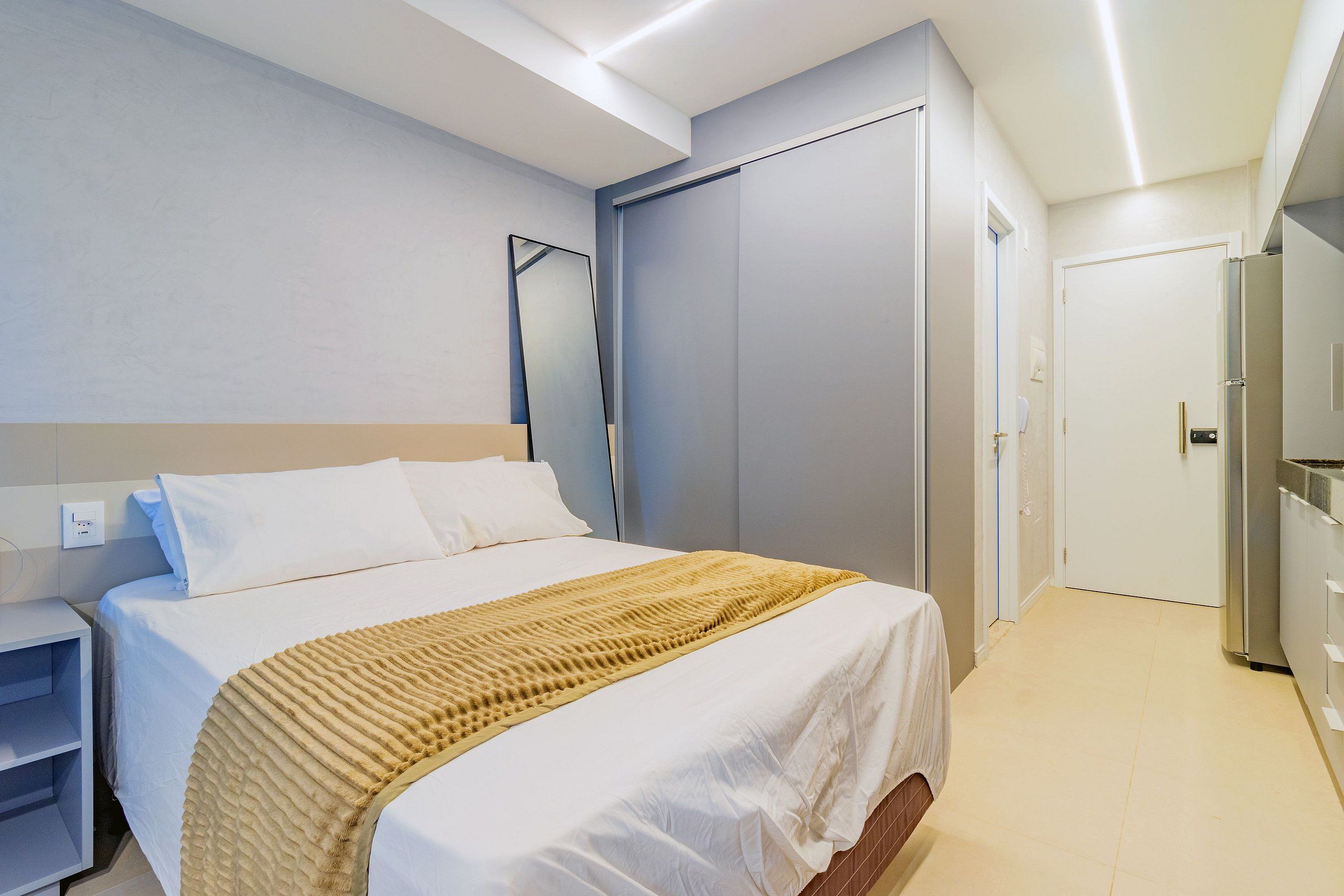Habitación de hotel con cama, armario, espejo y kitchenette.