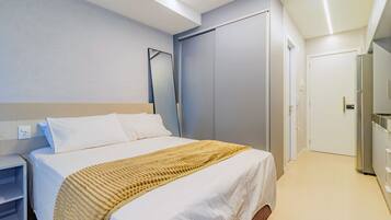 Habitación de hotel con cama, armario, espejo y kitchenette.
