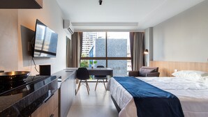 Una camera d'albergo con un letto, una scrivania con una sedia, una televisione e una finestra che offre vista sulla città.