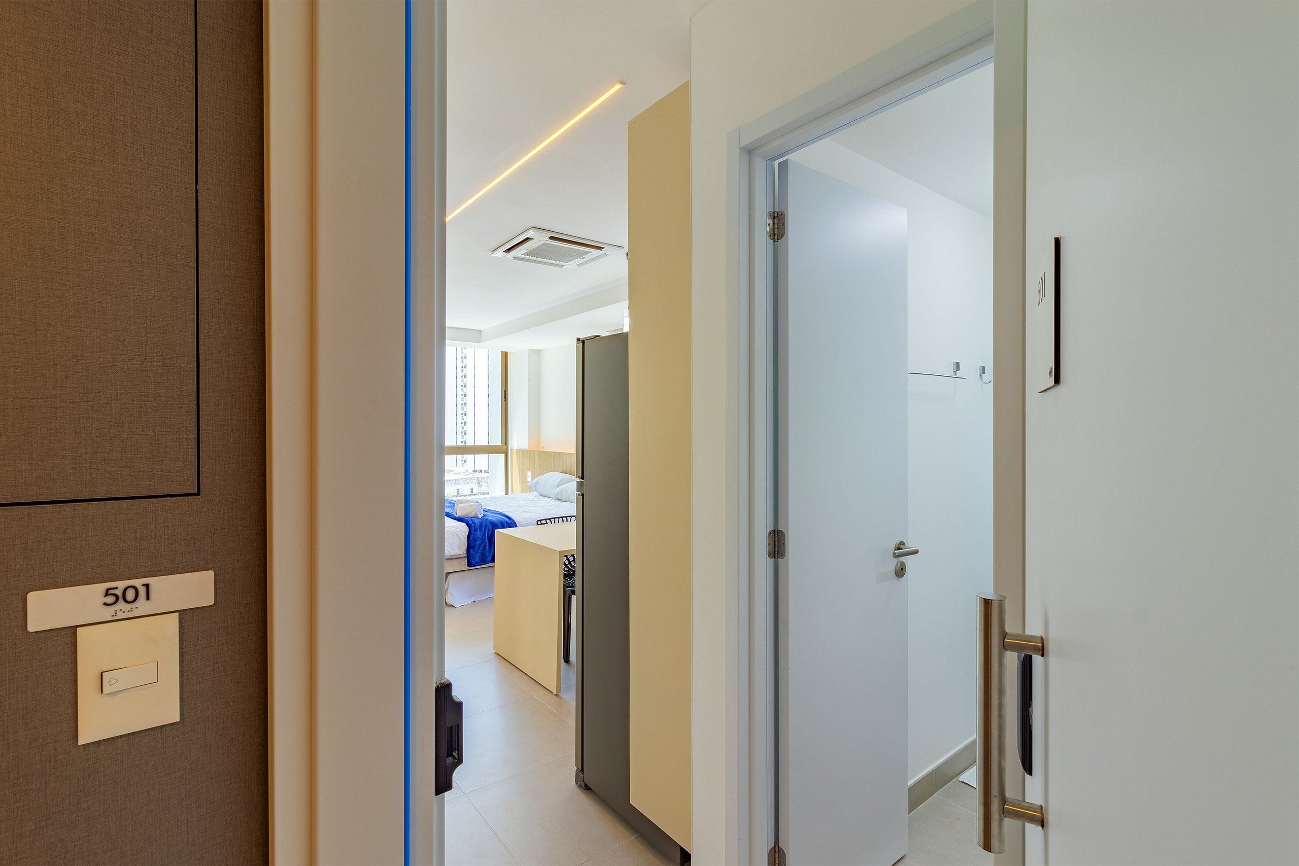 Corredor de hotel com o número do quarto 501 visível, uma cama e um banheiro com chuveiro.