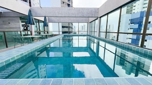 A modern indoor swimming pool with clear glass walls, a tiled floor, and a view of city buildings. - Rooftop.470 Recife by Carpediem (Recife)
