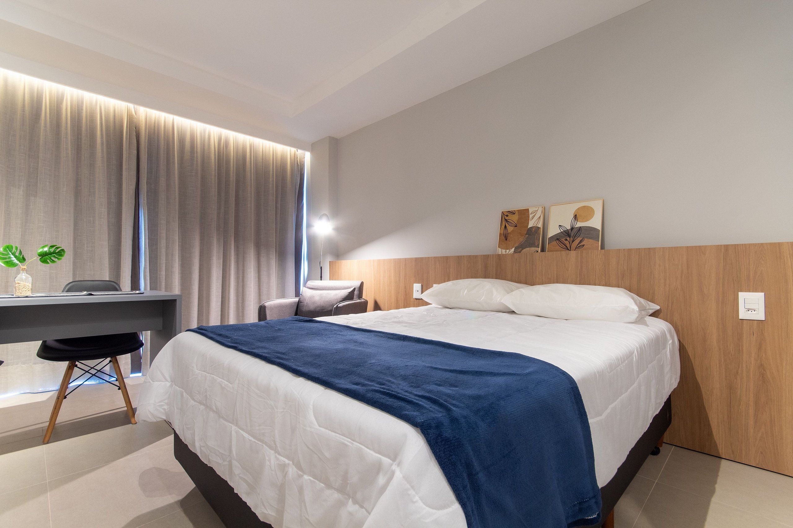 Quarto de hotel moderno com cama, escrivaninha, cadeira e obras de arte na parede.