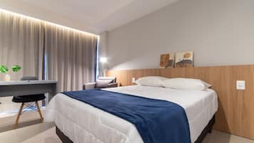 Quarto de hotel moderno com cama, escrivaninha, cadeira e obras de arte na parede.
