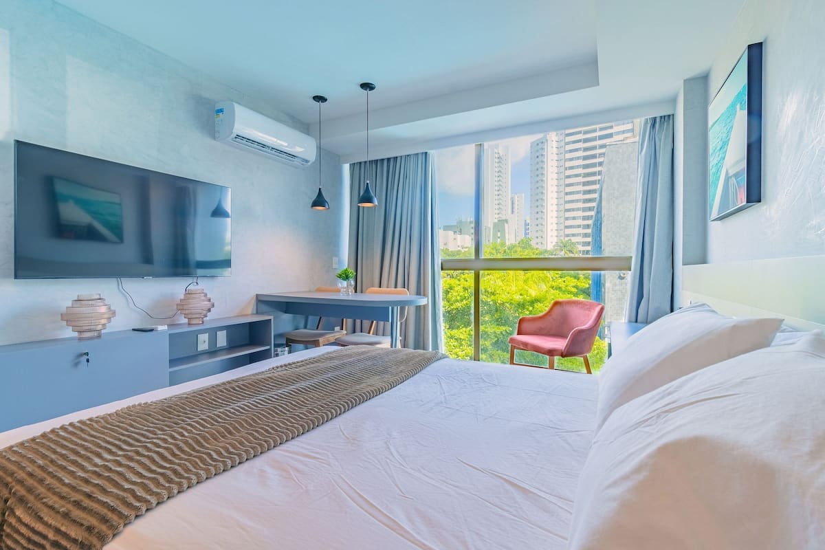 A modern hotel room with a large bed, a desk, a chair, and a TV mounted on the wall.