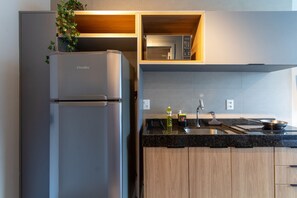 Une cuisine moderne dotée d’un four à micro-ondes encastré, d’un réfrigérateur en acier inoxydable, de meubles en bois et d’un plan de travail en granit.