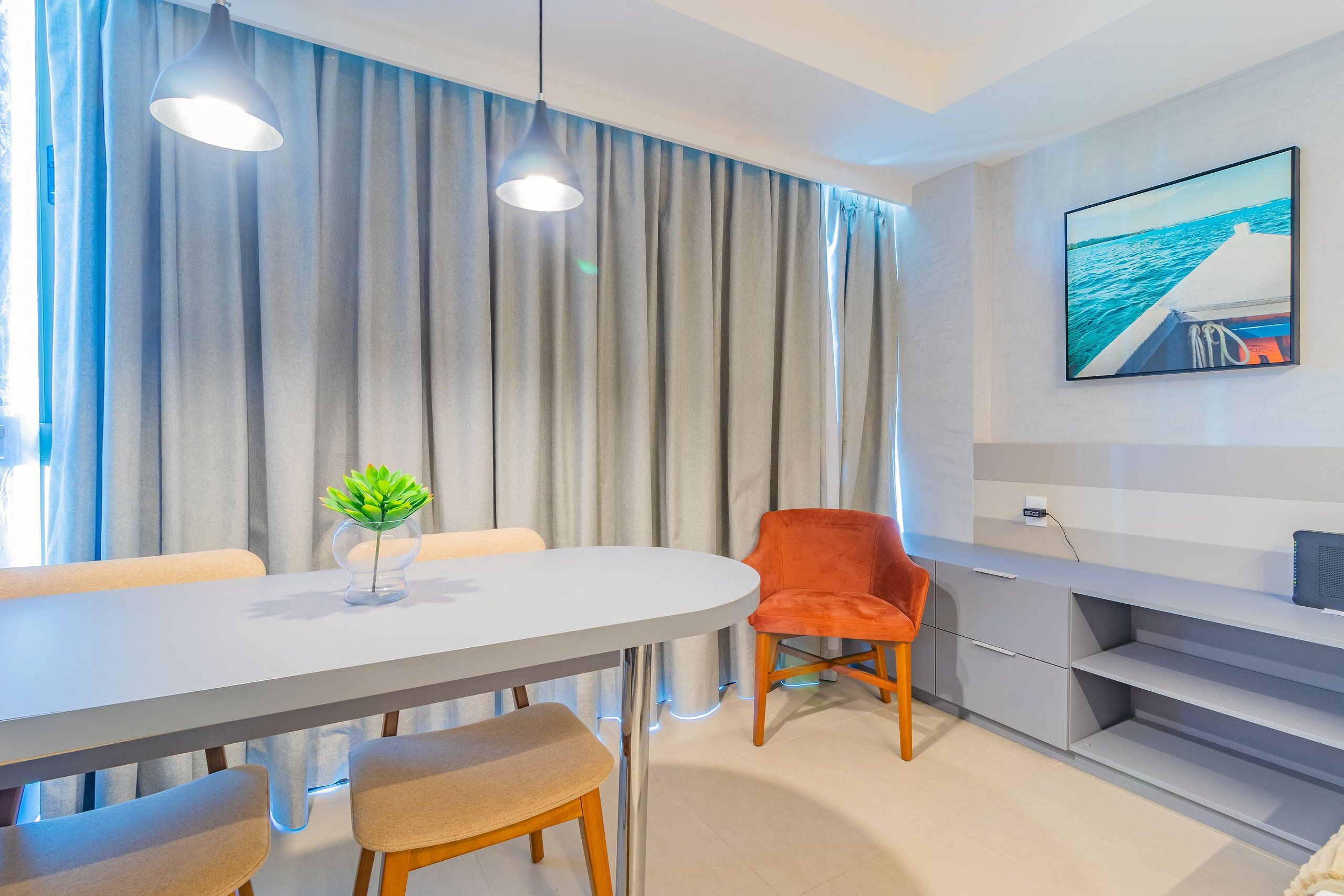 Uma zona de refeições moderna com uma mesa branca, cortinas cinzentas e uma cadeira vermelha.
