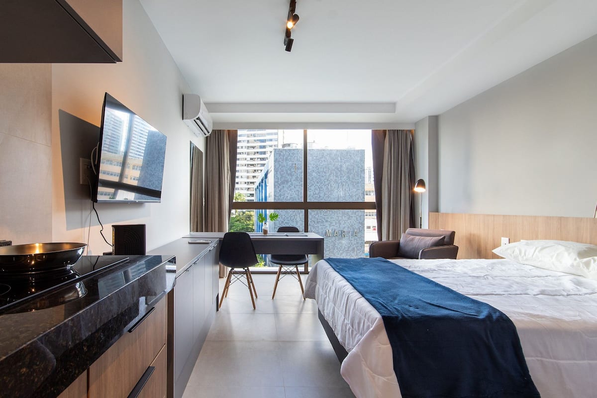 A hotel room with a bed, a desk with a chair, a TV, and a window with a city view.