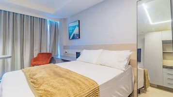 Habitación de hotel con cama, una silla roja, escritorio, espejo y un cuadro en la pared.