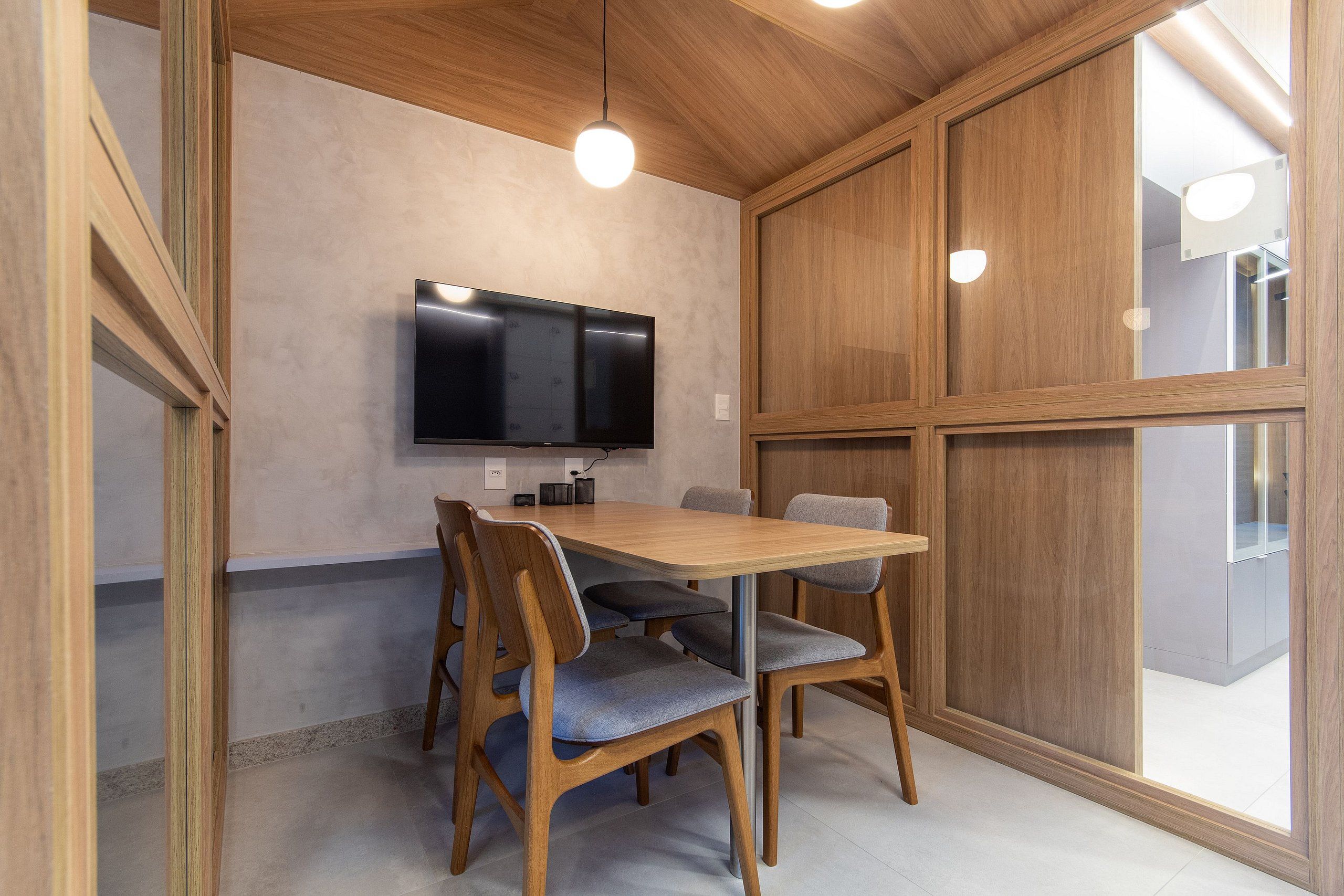 Uma área de refeições com mesa e cadeiras de madeira, uma TV de tela plana na parede e uma janela grande.