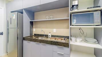 Uma cozinha compacta com geladeira, micro-ondas e cafeteira no balcão.