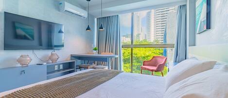 A modern hotel room with a large bed, a desk, a chair, and a TV mounted on the wall.