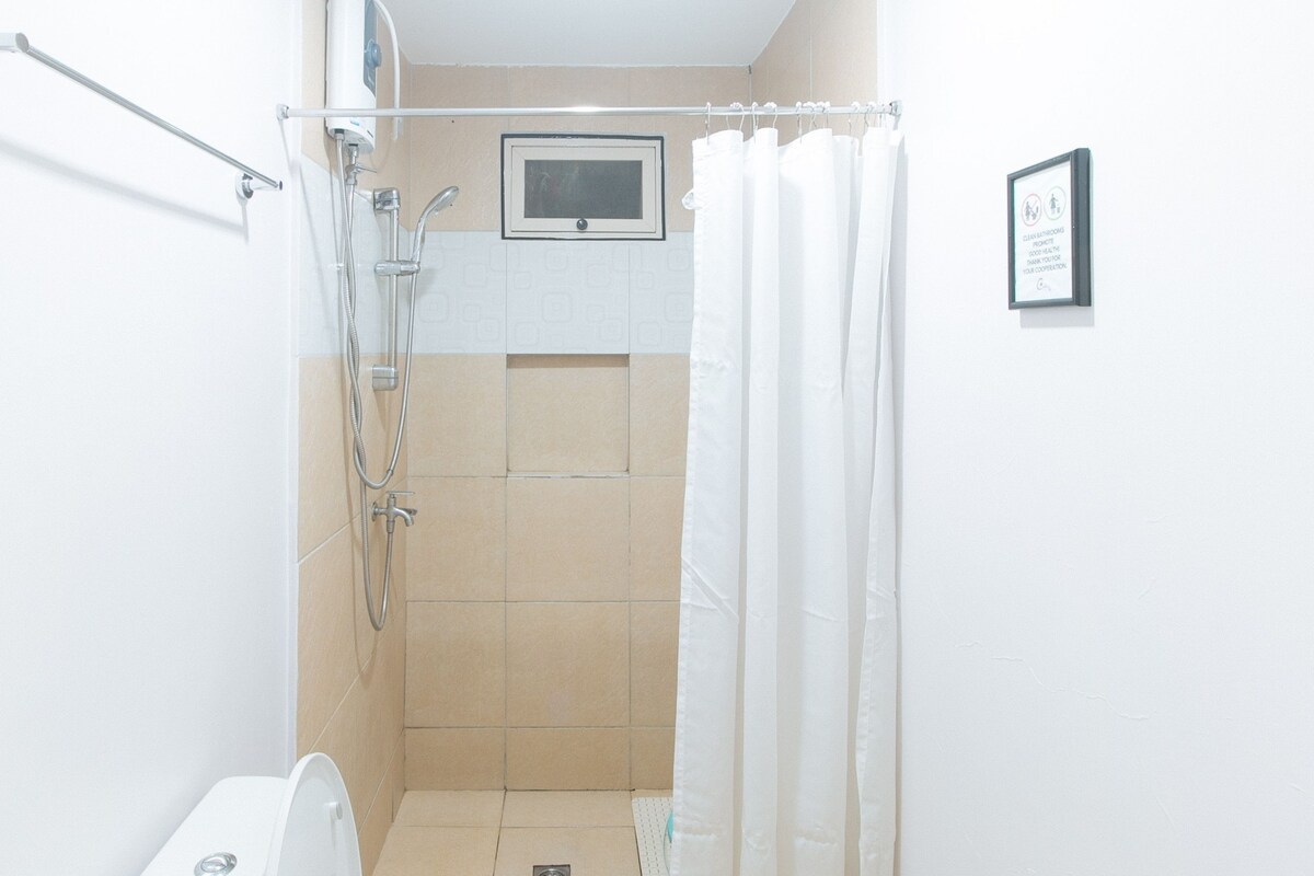 A shower area with a handheld showerhead, a wall-mounted control panel, and a white curtain.