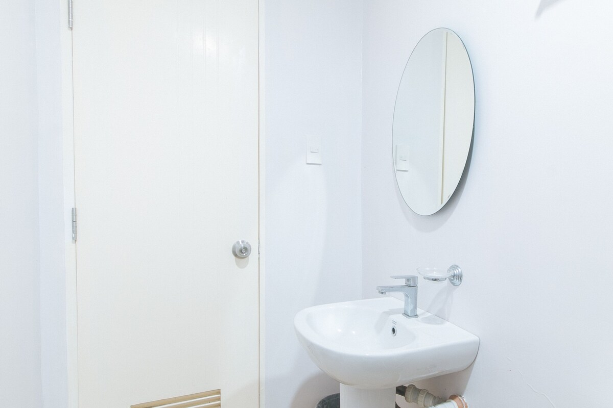 A white bathroom with a door, a round mirror, and a pedestal sink.