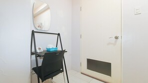 A small room with a black chair, a table with a blue basket, a white door, and a mirror on the wall. - Catlea Inn (Pasay)
