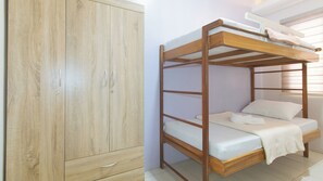 A bunk bed with a wooden frame and white bedding, a wooden wardrobe with two doors and a drawer, and a window with blinds. - Catlea Inn (Pasay)