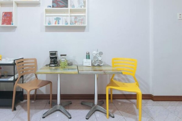 A dining area with a table and two chairs, one yellow and one brown, with a coffee maker and a small white appliance on the table. - Catlea Inn (Pasay)