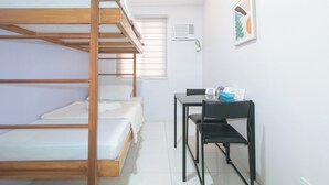 A dormitory room with bunk beds, a desk, a chair, and a small table with items on it. - Catlea Inn (Pasay)