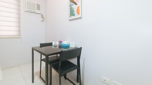 A small, clean room with a table and chairs, a window with blinds, a wall-mounted air vent, and a framed picture. - Catlea Inn (Pasay)