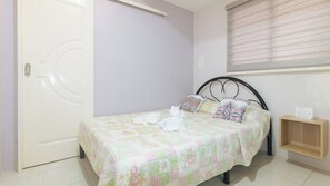A single bed with a floral bedspread, a bedside table with a lamp, and a window with blinds. - Catlea Inn (Pasay)