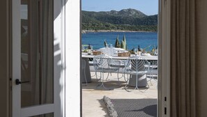 An open door leading to an outdoor dining area with a view of the sea and mountains. - The Icon - Tuerredda (Teulada)