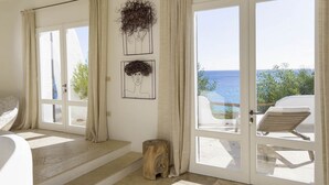A room with a large window overlooking the sea, a bed, a wooden stool, and two framed artworks on the wall. - The Icon - Tuerredda (Teulada)