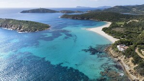 A coastal landscape with a beach, clear blue waters, and green hills. - The Icon - Tuerredda (Teulada)